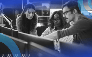 Three software developers collaborating while one points at the desktop screen.