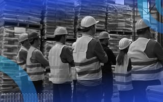 A group of workers in safety vests and hard hats stand in a warehouse