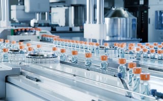 Several vaccine vials pass through a conveyor belt to represent biotechnology research and development.