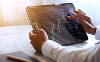 A close up of two hands holding a tablet with an fluctuating line graph on the screen to represent trading activity.