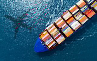 silhouette of a plane flying over a cargo ship