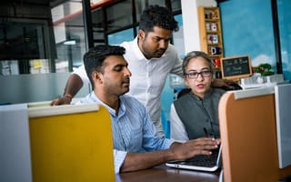 Three team members look at a computer screen together, discussing its contents.