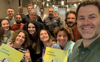 Udemy employees pose for a group selfie holding signs that read “Always Learning.”