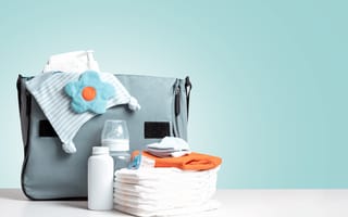 A baby bottle and stack of diapers sit in front of a blue diaper bag.