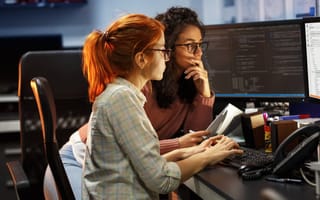 Two engineers look at a computer monitor to review the work being done on an AI project.