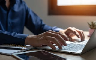 A close up of a pair of hands typing on a laptop keyboard at a desk.