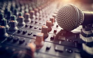 A close up of a microphone lying on top of a sound mixing board.