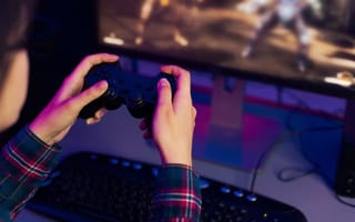 A close up of a pair of hands holding a game controller in front of a PC monitor.