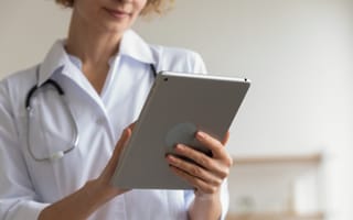 A photo of a doctor wearing a white coat and stethoscope holding a tablet in their hands.