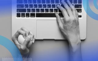 An aerial view of a pair of hands on a laptop keyboard, the right hand typing while the left hand squeezes a stress ball.