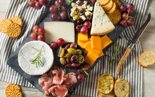 A charcuterie board with a big wheel of brie on top of a blue striped tea towel.