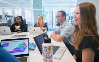 Datadog team members meet in a conference room, laptops open and smiling.