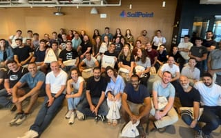 SailPoint employees seated in a large group in front of a branded office wall.