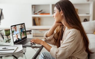 A woman in a home office sits in front of a laptop with a video conference call featuring four other professionals on the screen.