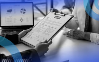 A recruiter looks at a resume on a clipboard as a candidate in a tie sits across the table