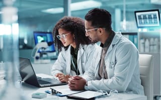 Two cancer researchers examine findings on a laptop computer screen in a laboratory.