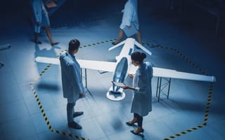 Two professionals in white lab coats stand over an aircraft model.