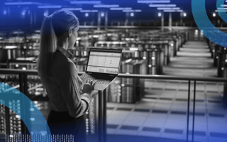 An engineer looks at a laptop in a room full of servers