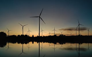 A field of wind turbines sit in water with the setting sun in the background.