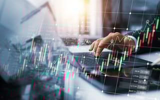 A close up of an investor's hand typing on a laptop keyboard overlaid by a red and green chart to represent financial market activity.