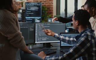 A team of developers is pictured looking at code on a desktop computer monitor.