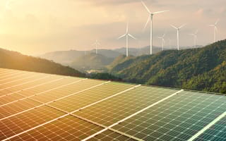 Solar panels are displayed in a rural outdoor setting with multiple wind turbines in the background.