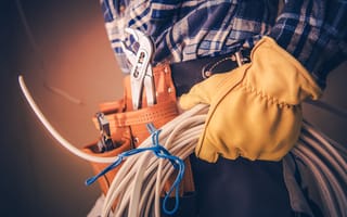 A close up of a service worker's hand wearing a globe and holding cables is depicted.