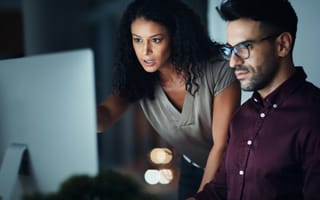 Two software developers look at a desktop computer monitor as they work on code.