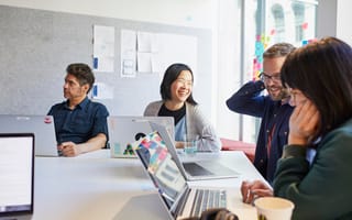 A group of Atlassian employees collaborate around a table with laptops open.
