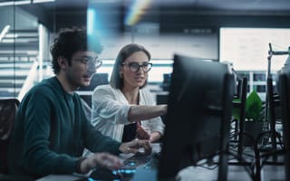 Two AI engineers look at data on a computer monitor screen while collaborating on a project in the office