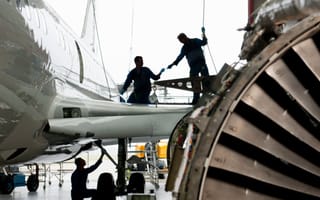 Two aerospace workers are pictured working on the wing of an aircraft.