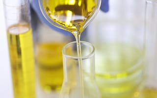 A close up of a gloved hand pouring oil from one glass container into another.