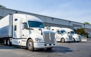Three white cargo trucks are parked side-by-side in front of a warehouse.