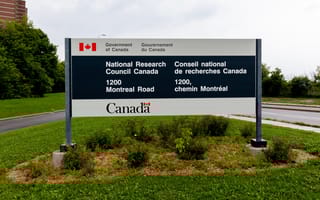 Sign for the National Research Council Canada, displaying contact info in English and French, set against greenery and a cloudy sky.