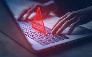 Hands typing on a laptop keyboard with a glowing red warning triangle and exclamation mark overlay.