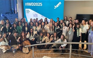 A large group of HERE Technologies women team members pose for a group photo while flexing their arms during the company’s 2025 Ignite event