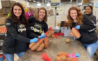 Three McCain Foods team members holding bags of potatoes while wearing company-branded T-shirts in a packing facility.