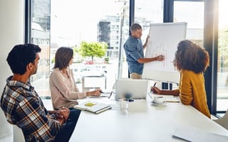 A salesperson presents sales growth metrics on a whiteboard while three of his colleagues watch