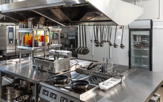 A restaurant kitchen is pictured featuring pans, ladles, a stove and food prep space.