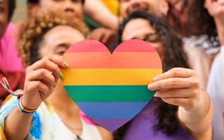 A group of people celebrating Pride Month, with two individuals holding a rainbow heart at the center
