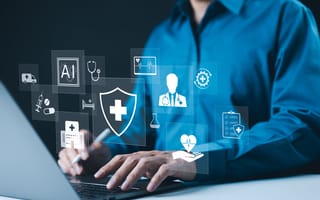 Person in a blue shirt uses a laptop, surrounded by floating medical icons like a shield, doctor and heart, conveying a digital healthcare theme.