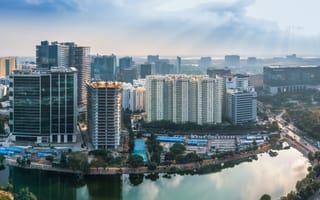 Aerial view of a modern cityscape with high-rise buildings, a reflective pond and sunrays piercing through clouds.