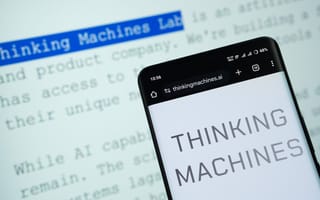 Thinking Machines logo on a smart phone in front of a computer screen. The Thinking Machines website is visible in the background.