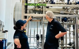 Two employees wearing navy uniforms sand in an industrial environment.