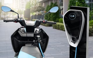 A scooter sits next to an electric vehicle charger.