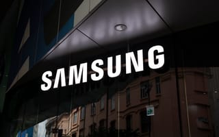 Illuminated Samsung logo on a storefront, with reflections of urban buildings on glass.