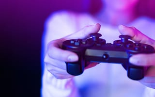 Hands holding a gaming controller, illuminated by vibrant purple and blue lighting.