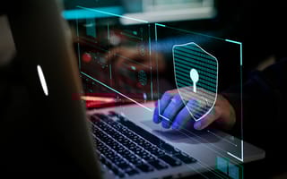 A person types on a laptop, with digital security graphics overlaying the image. A shield with a keyhole symbolizes cybersecurity themes.