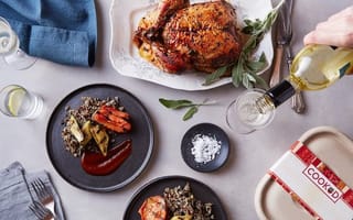 A decadent table setting featuring a roasted poultry, white wine, and a linen table cloth.