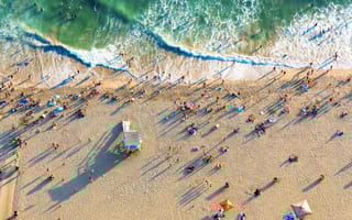 Aerial view of a beach spotted with people on the sand as foaming waves roll towards them.